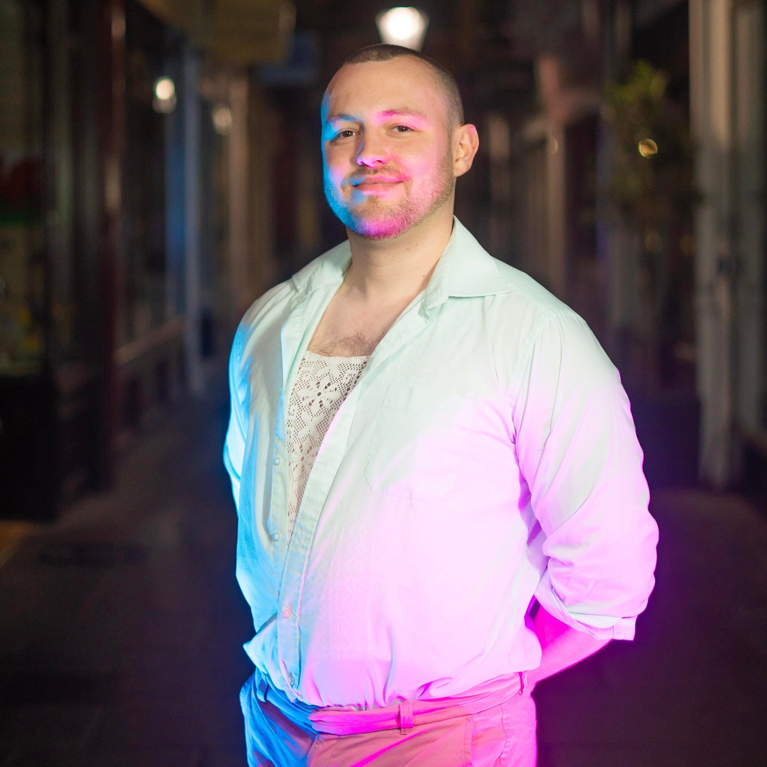 Daniel Huw Bowen stood in the Royal Arcade, facing the camera, lit in blue and pink.
