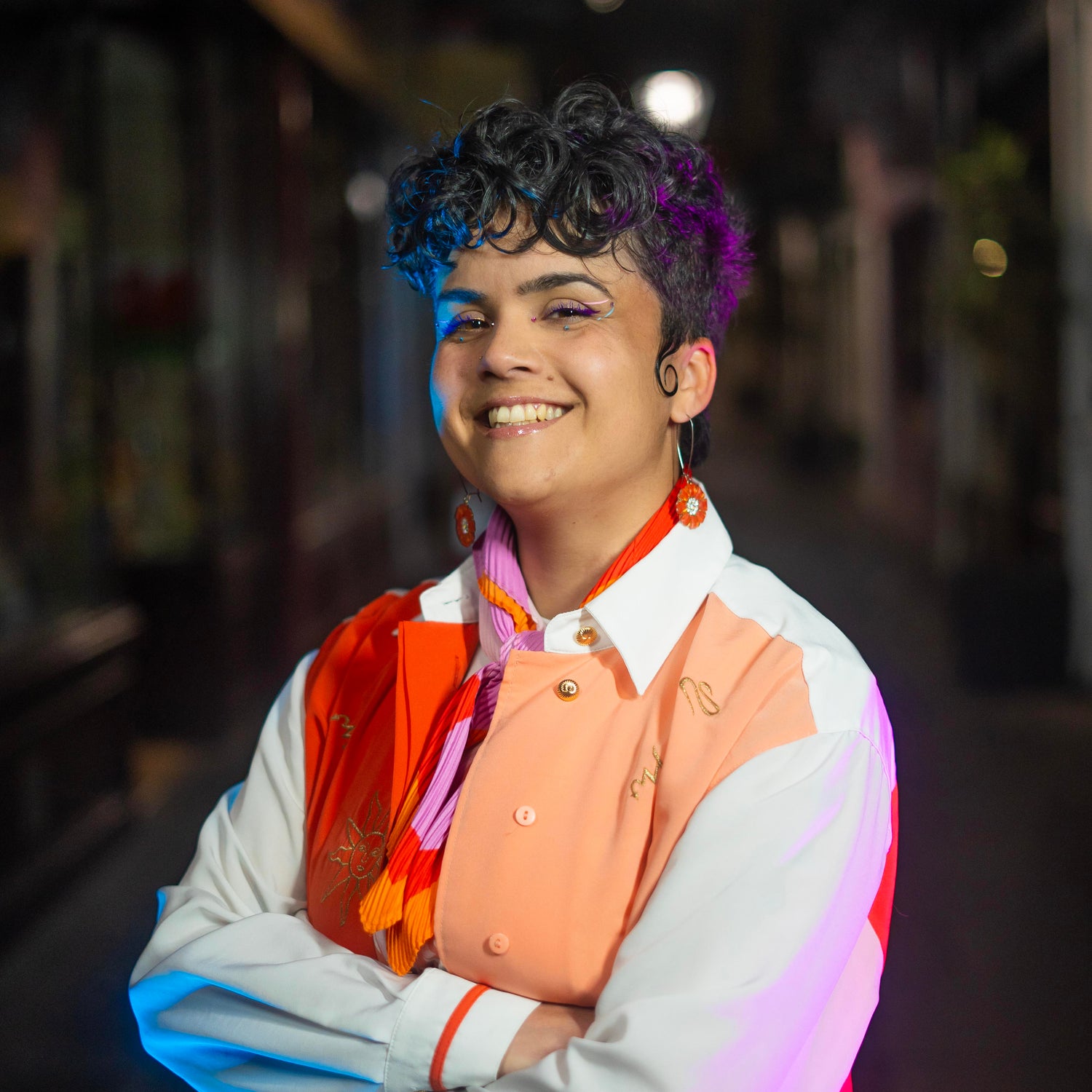 Billie smiling, lit up in blue and pink, in a dimly lit arcade.