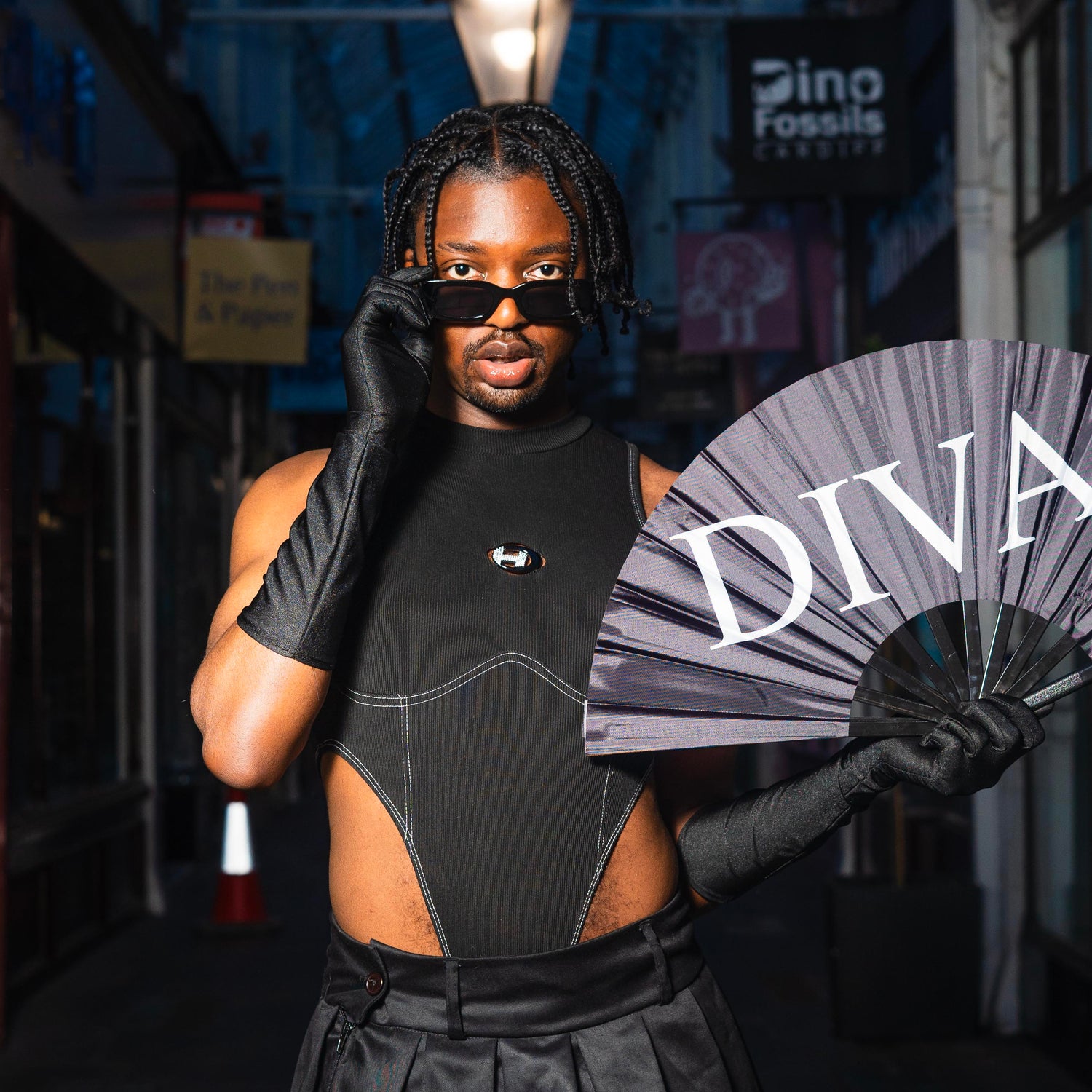 Kabambi in a dimly lit Arcade, holding a fan that says 'Diva'.