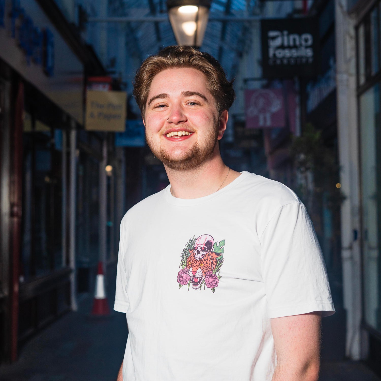 Leo, in a white t-shirt, smiling in a dimly lit arcade.