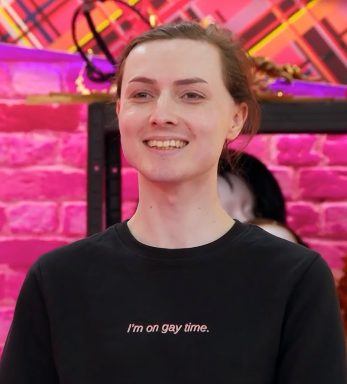 Marmalade on Drag Race UK in the werk room wearing the "I'm on gay time." jumper. It is a black jumper that says "I'm on gay time." in red and white lettering.