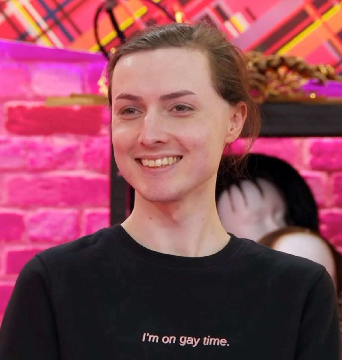 Marmalade on Drag Race UK in the werk room wearing the "I'm on gay time." jumper. It is a black jumper that says "I'm on gay time." in red and white lettering.