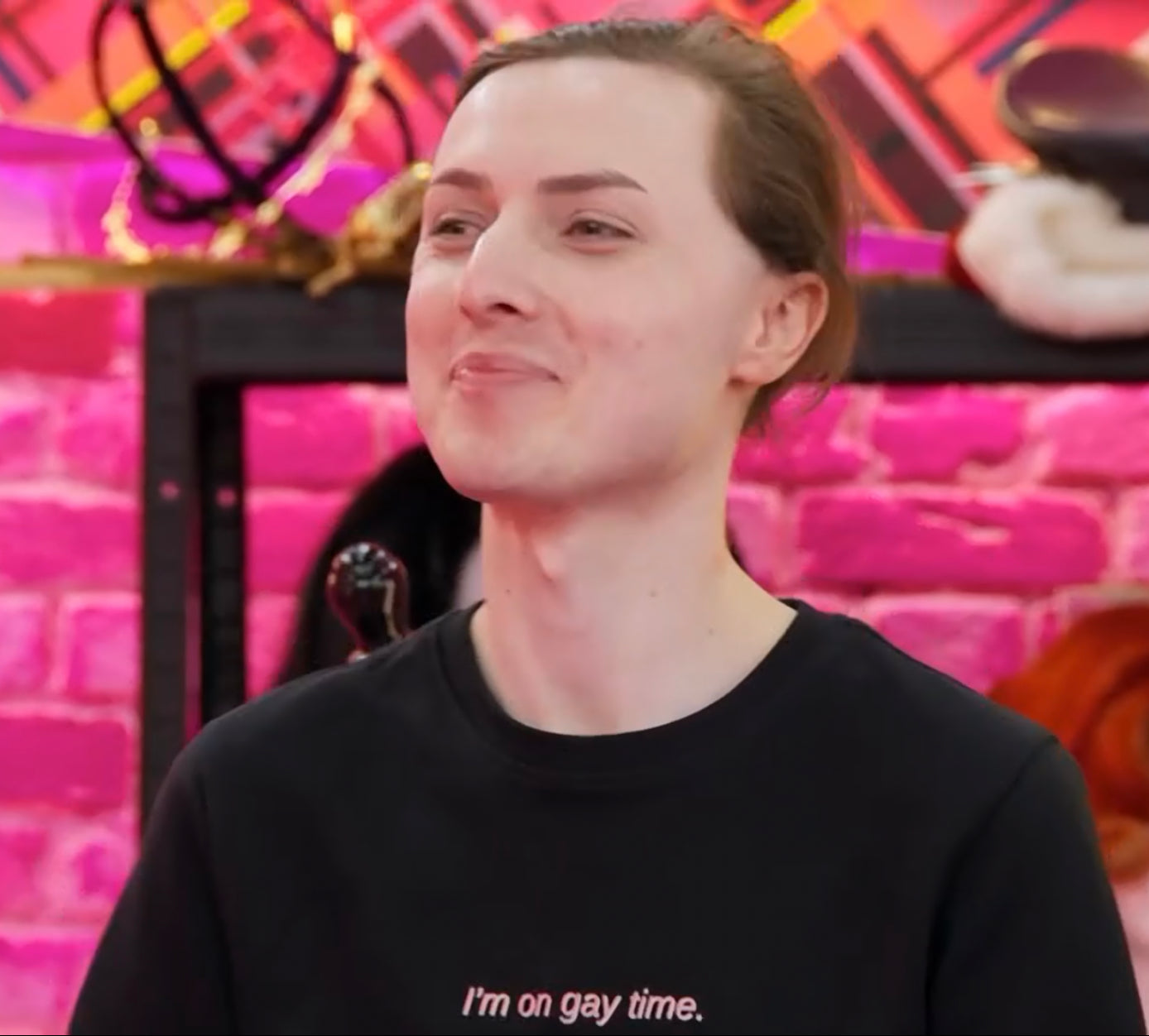 Marmalade on Drag Race UK in the werk room wearing the "I'm on gay time." jumper. It is a black jumper that says "I'm on gay time." in red and white lettering.