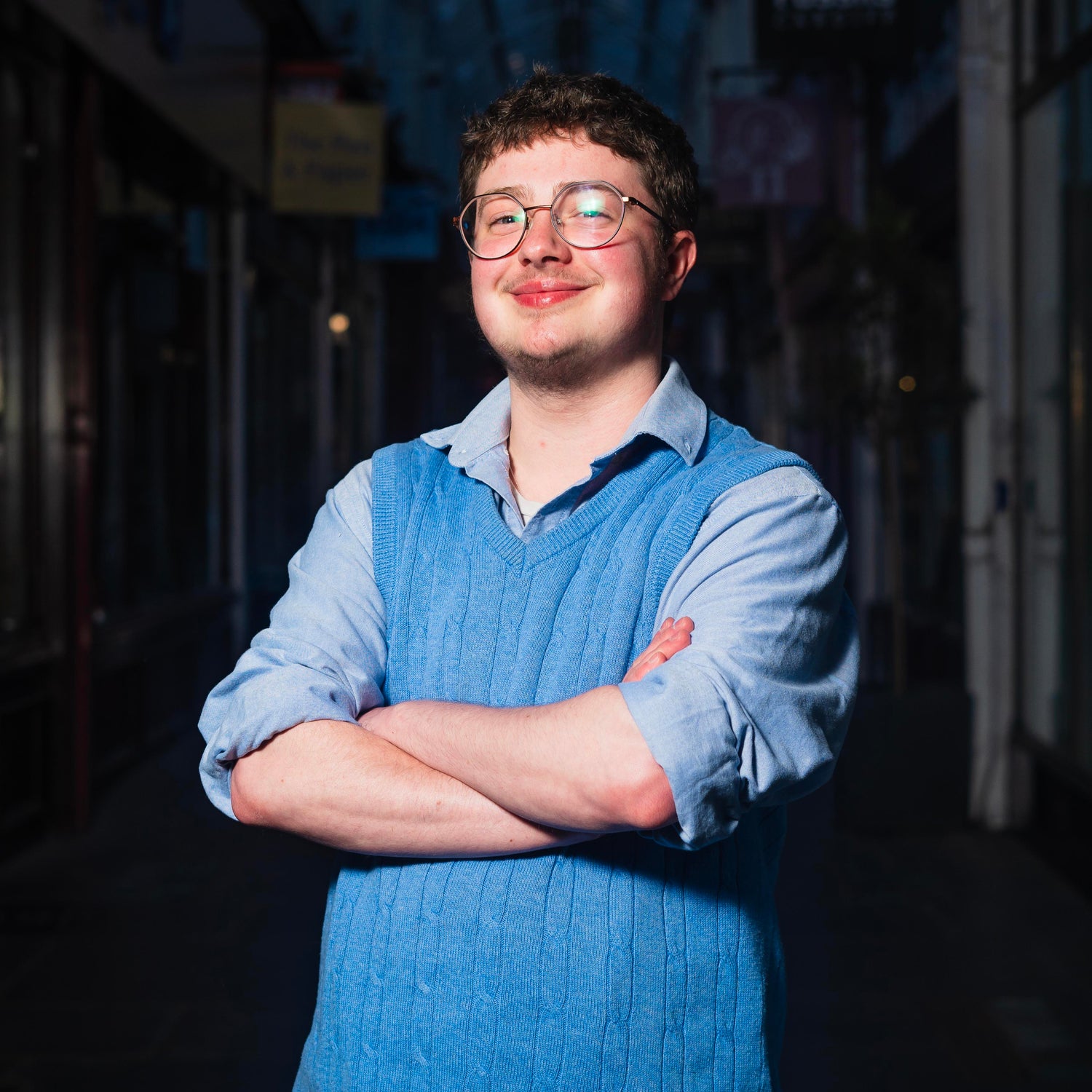 Milo, in a blue shirt and vest, smiling and posing with his arms crossed.