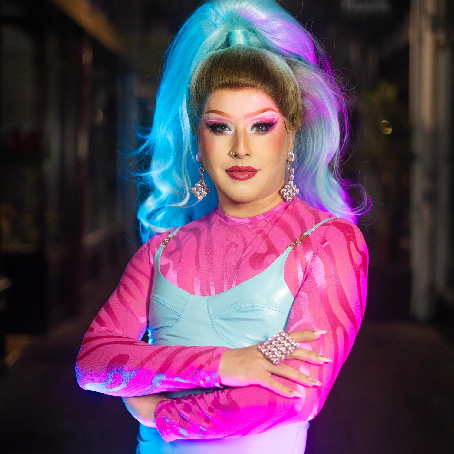 Polly Amorous, in a blue wig and pink and blue outfit, stares directly at the camera.