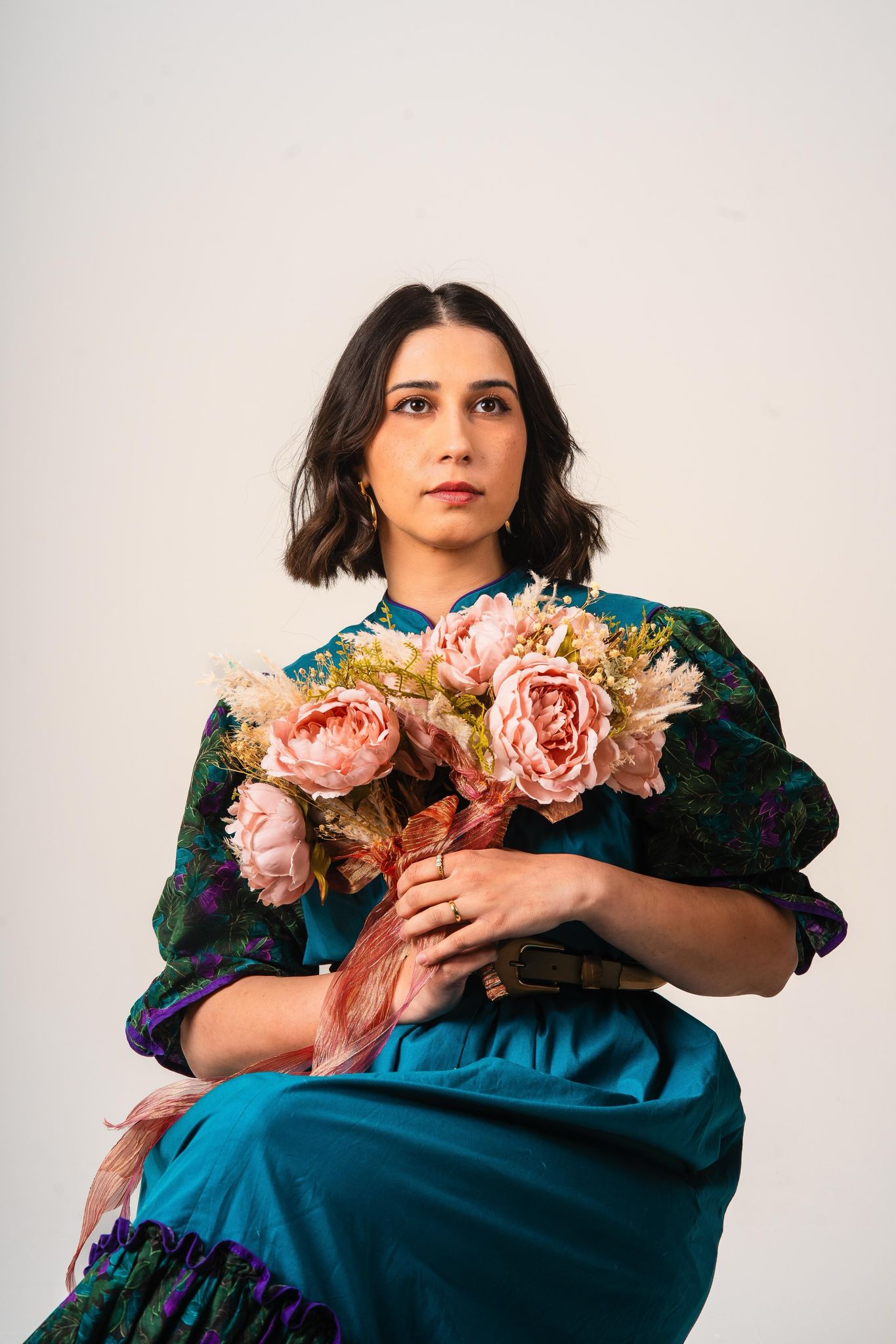 Light background featuring Priya Hall staring into the distance, whilst wearing a blue dress and holding a bouquet.